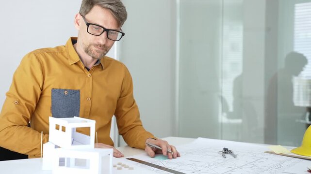 Architect working on architectural blueprint and scale model, designing and planning a new building project, focusing on engineering details and construction plans in a modern office