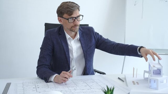 Thoughtful architect planning new project, analyzing building blueprints and architectural model, developing innovative design solutions in modern office workspace