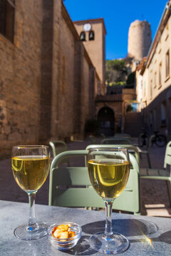 Two glasses of white wine on a table on a scenic street with the historic church and the medieval Barbarossa Tower in the background, Gruissan, Occitanie, France