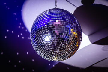 Fototapeta premium Shiny mirror disco ball with colorful reflections at nightclub. Neon sphere with bright rays, hanging on ceiling, night party background