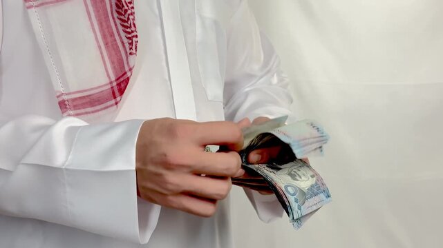 Saudi man wearing traditional thobe counting five hundred riyal banknotes close up.