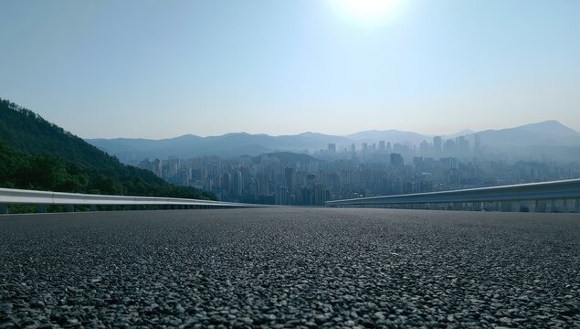 Empty highway curves toward a hazy, distant cityscape and lush green mountains