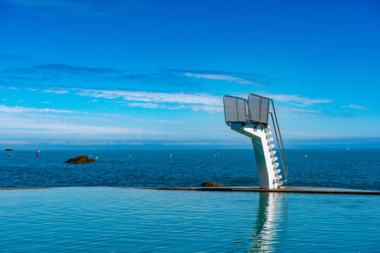 Diving platform at tidal pool with offshore wind turbines on horizon, Saint-Quay-Portrieux