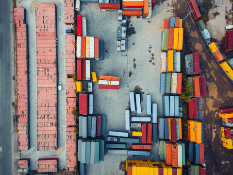 Warsaw, Poland - 15 September 2024: Aerial view of colorful cargo containers stacked in a logistics terminal with rows of shipping units and muddy ground.