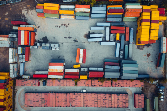 Warsaw, Poland - 15 September 2024: Aerial view of colorful cargo containers stacked in a logistics terminal with trucks and trailers on a grey asphalt surface.