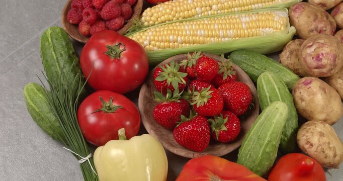Various fresh healthy products on a gray table. Close-up footage of  corn, strawberries, cucumbers, tomatoes, green onions, potatoes, raspberries, dill, sweet peppers on a rotating table.