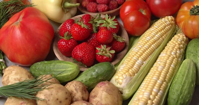 Various fresh healthy products on a gray table. Close-up footage of  corn, strawberries, cucumbers, tomatoes, green onions, potatoes, raspberries, dill, sweet peppers on a rotating table.