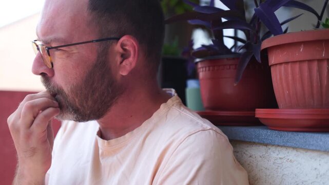 An anxious handsome man with a beard, biting nails on a terrace, making it a bad habit routine