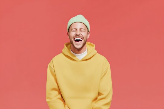 Happy young man laughing in yellow hoodie and green beanie over a solid red background for cheerful inclusive fashion marketing and lifestyle advertising campaigns