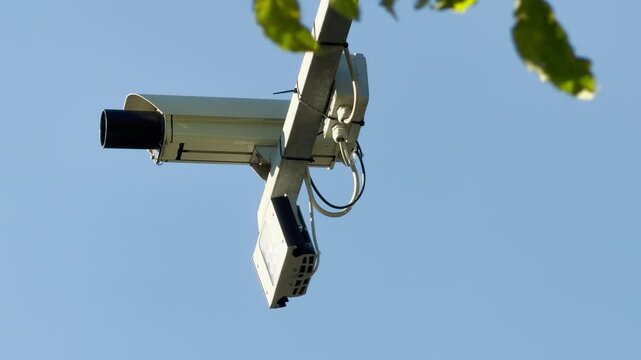 The surveillance camera watches over the road under a clear sky. The steady hum of passing cars fills the environment.