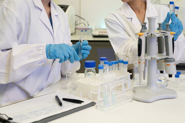 Fototapeta premium Two Scientists in White Lab Coats Working with Test Tubes and Pipettes in a Research Laboratory