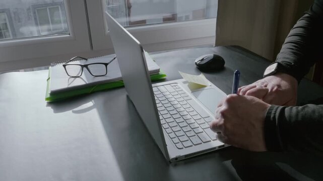Person writing a note on a sticky pad at home office desk