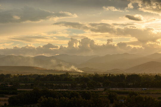 Majestic sunset over rolling hills with clouds and smoke in the distance