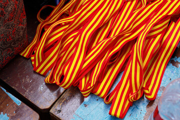 A pile of vibrant red and yellow striped ribbons clustered together on top of a weathered, dark wooden bench or surface