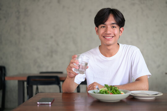 Young Asian non-binary man smiling holding glass of water looking at camera