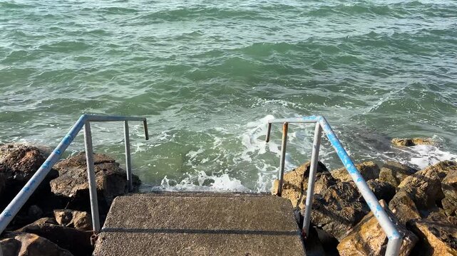 Old staircase leading to the sea, waves washing coastal steps. Weathered staircase descending into the sea, waves washing steps, Mediterranean Sea