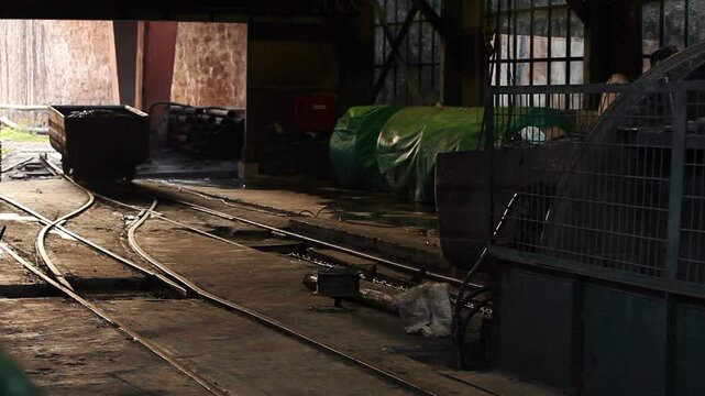 Dark industrial scene of heavy metal mining carts moving on railway tracks inside an old mine facility.