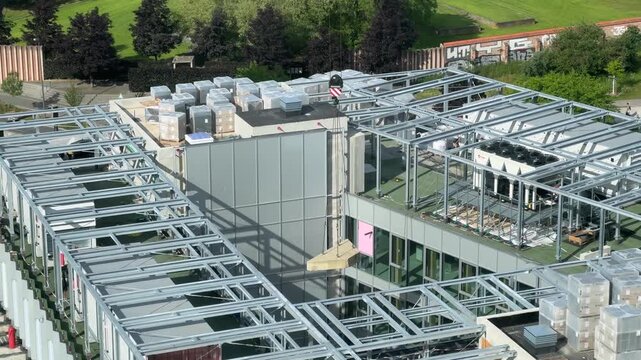 High-angle view of a construction crane lowering a heavy precast concrete slab onto the steel rooftop framework of a commercial building