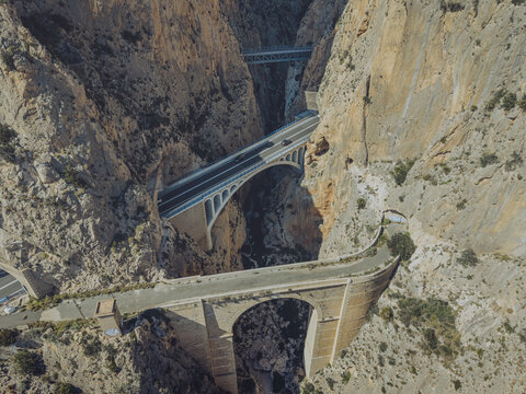 Aerial view of the historic Ponts del Mascarat bridges spanning the deep rocky canyon with modern road infrastructure and rugged cliffs in Altea, Comunidad Valenciana, Spain.