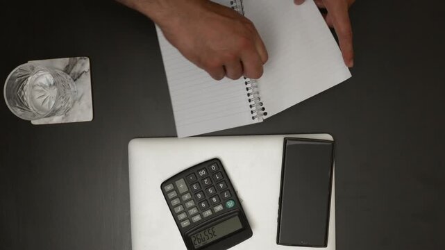 Overhead flat lay of male hands turning the page of a spiral notebook on an office desk, fresh start concept.