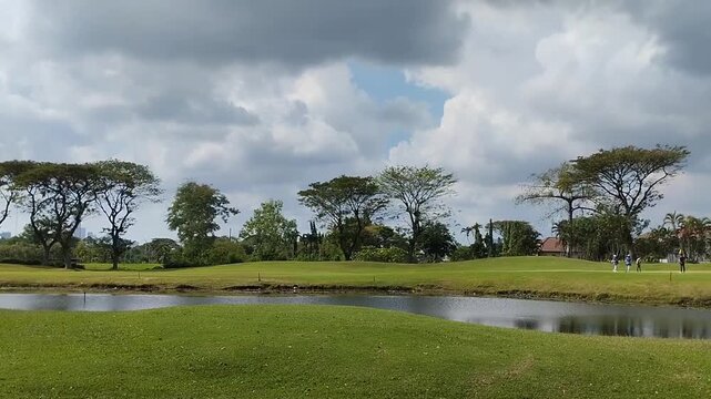 A lush green golf course with shady trees and manicured lawns under sunny skies. A serene tropical golf course