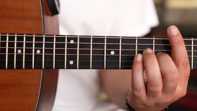 Close-up shot of a male musician's hands playing chords on an acoustic guitar fretboard.