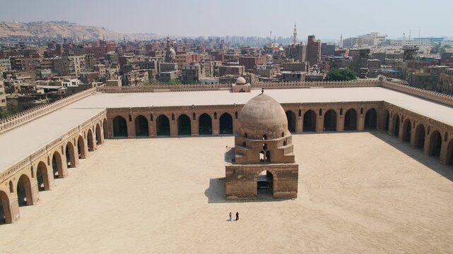 Courtyard of Ibn Tulun Mosque, oldest mosque located in Islamic Cairo, Egypt. Vast historic mosque courtyard surrounded by arcaded colonnades and dominated by a central domed ablution fountain.