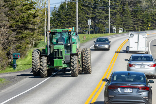 Gaspesie, Canada, 30 May 2026 : A green John Deere tractor drives on a paved road alongside passenger cars under a clear sky.