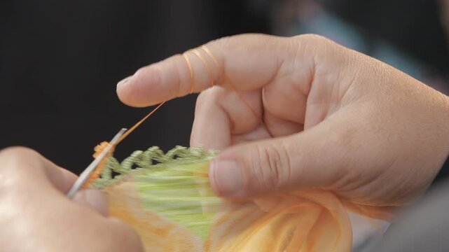 Close-up shot of a woman's hands crocheting traditional Turkish needle lace (oya) on the edge of a colorful fabric.
