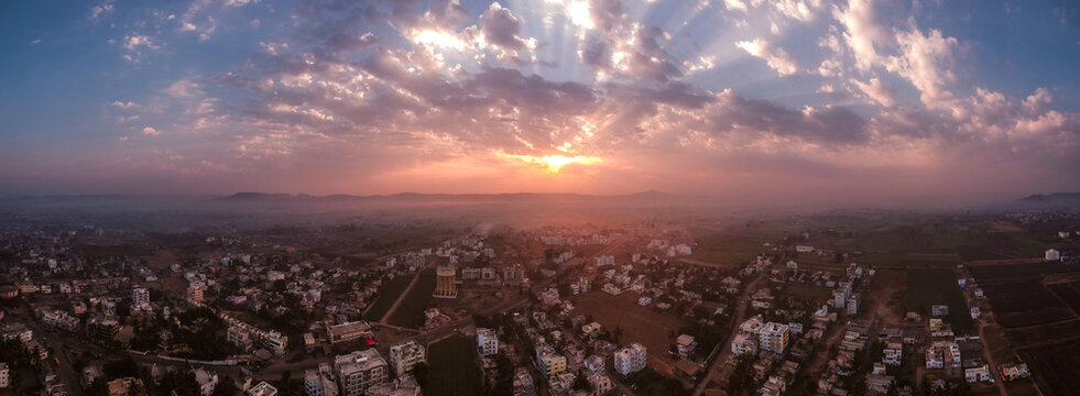 Aerial view of the town of Karad at sunset, featuring urban buildings, roads, and surrounding agricultural fields under a dramatic cloudy sky in Karad, Maharashtra, India.