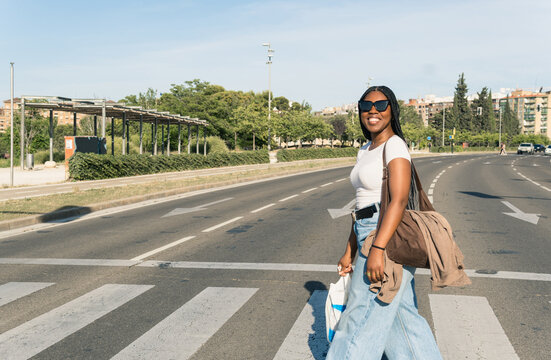 Smiling young woman crossing street on sunny day