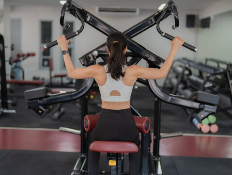 Young asian woman training legs on squat machine in fitness gym.