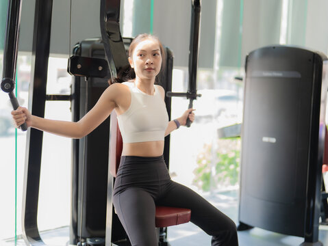 Young asian woman training legs on squat machine in fitness gym.