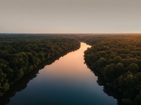 Aerial view of calm river reflecting warm sunset sky winding through dense green forest trees