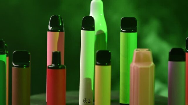 Rotating display of colorful disposable electronic cigarettes under shifting neon lights.