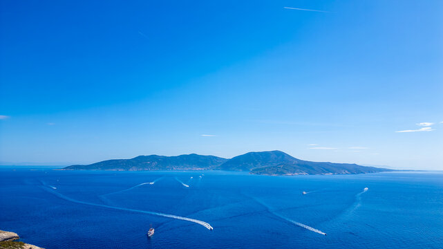 Aerial view of the island of Bisevo surrounded by the deep blue Adriatic Sea with several boats leaving white wakes, under a clear sky in Bisevo, Split-Dalmatia County, Croatia.