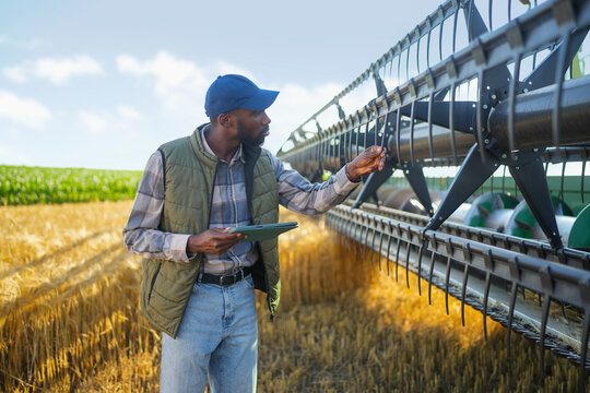Farmer inspecting harvesting equipment while reviewing operational data on a tablet.
