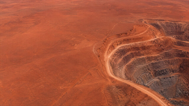 Aerial view of an open pit mine in a red desert landscape. Massive excavation site for mineral resource extraction. Industrial surface mining operations in arid remote wilderness.