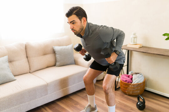 Man exercising at home, doing bent-over rows with dumbbells in his living room, focusing on strength training