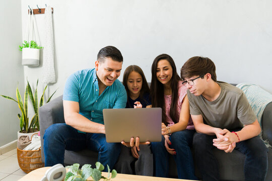 Latin family bonding at home, enjoying online content on a laptop while relaxing on the sofa