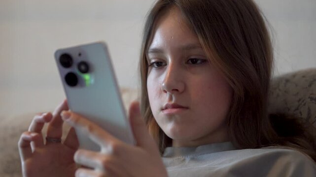 Pretty young girl sitting on cozy couch, using mobile apps in living room.