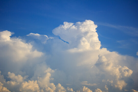 A massive, billowing cumulus cloud catches the warm golden light of late afternoon against a clear blue sky