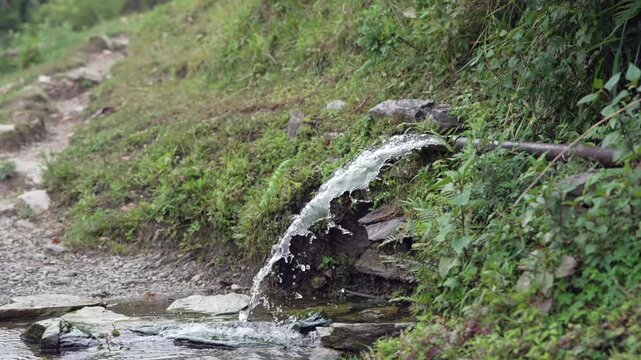Fresh mountain spring water flowing from a pipe into a stream