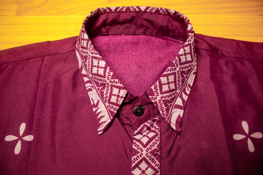 Flat-lay view of a dark maroon button-up shirt featuring traditional Indonesian batik patterns on the collar and placket with elegant petal-shaped motifs on the chest