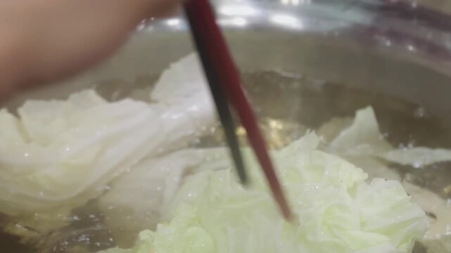 Cooking shabu shabu hot pot with chinese cabbage and sliced pork in boiling broth, close up Asian cuisine 4K video