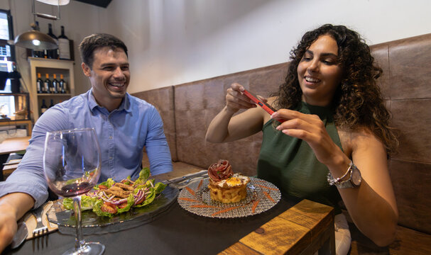 A woman takes photos of her plate of food whilst having dinner with her husband