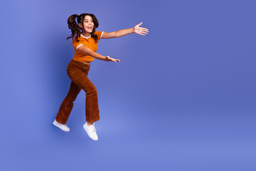 Happy young girl jumps in orange top and brown pants against violet background for lifestyle...