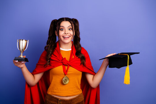 Young female student celebrates first place with trophy and cap beside blue background