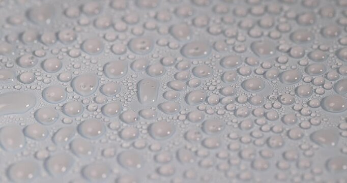 The liquid solidified on the surface, a transparent liquid in the shape of hemispheres on a blue plastic coating in side light with clear organic details and brightness.