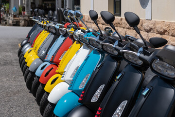 Colorful scooters lined up in a row, showcasing vibrant designs and sleek shapes, parked under bright sunlight, creating a lively urban atmosphere and inviting exploration © 18042011